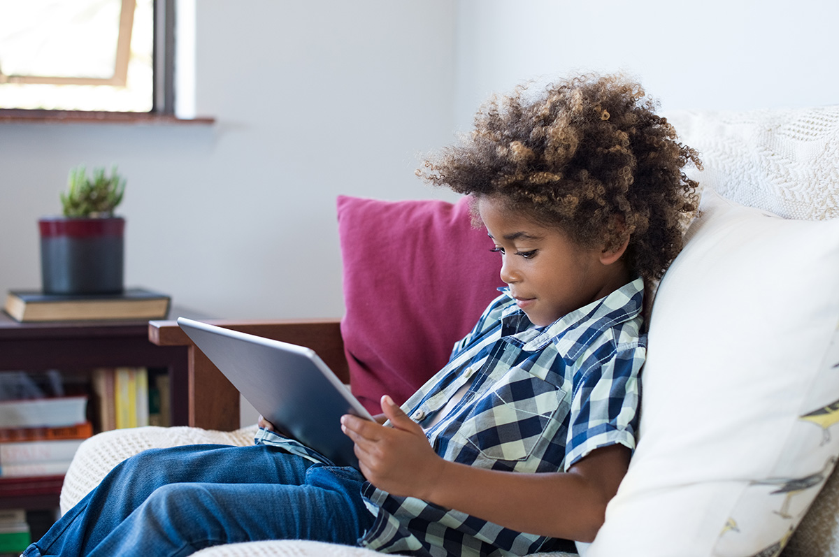 Little boy sitting on sofa and playing a game on digital tablet