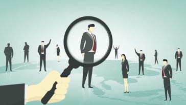 Businessmen standing on top of a globe. A larger hand holding a magnifying glass hovers the glass over one of the men.