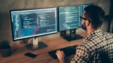 Image of a software developer working in front of two computer monitors.