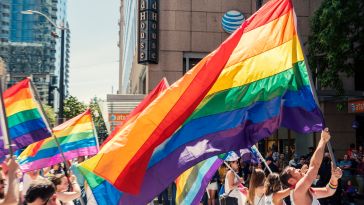 People walk through the street with the Pride flag held over their heads