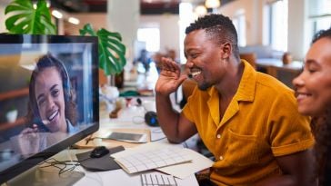 A man waves to his colleague on a video call from his office