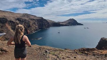 Partner Delivery Consultant Kaitlin Fox with her back to the camera, standing on a cliff overlooking water.