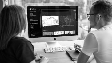 A woman and man sit at a Mac desktop