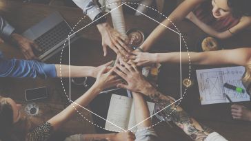 Eight hands in a circle over a table littered with books, notebooks and pencils.