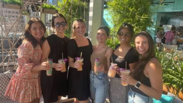 Six Navan employees — all women — with tropical drinks in hand pose for group photo