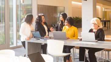 Five Liberty Mutual team members gather at a community table in Liberty Mutual’s common area with laptops, in discussion. 